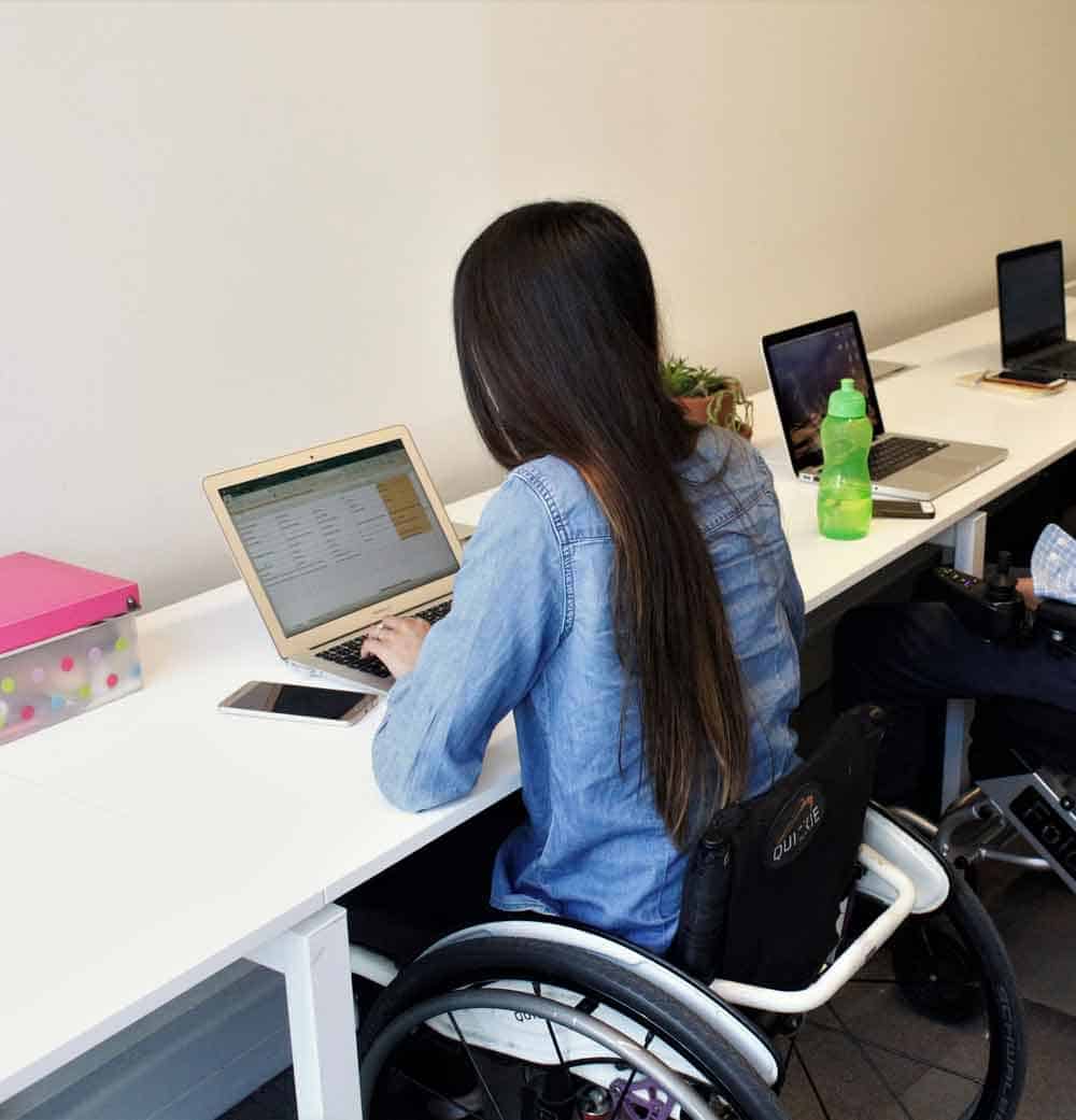 Una mujer en silla de ruedas trabajando en su escritorio con su computador.