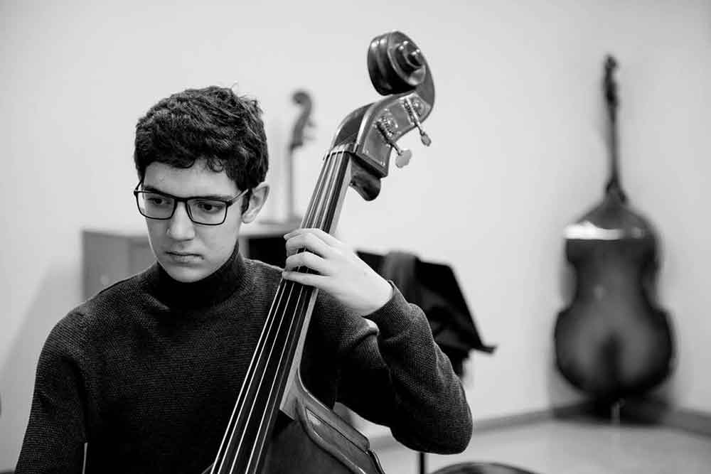 Un joven autista tocando contrabajo y con cara de concentración.