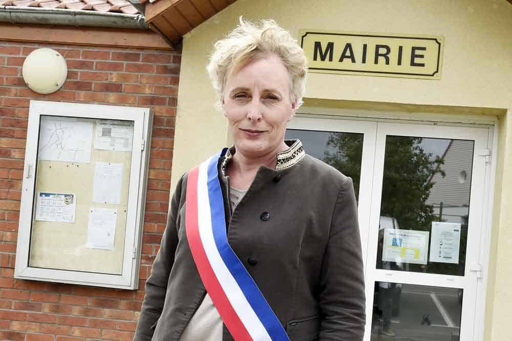 Aparece una mujer trans con una banda presidencial con los colores de Francia. Está afuera de la municipalidad donde trabaja.