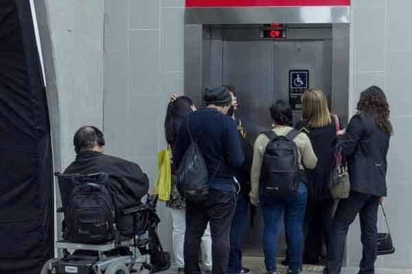Foto donde aparece una persona en silla de ruedas mirando como otras personas de pie y jóvenes, se suben antes que él.