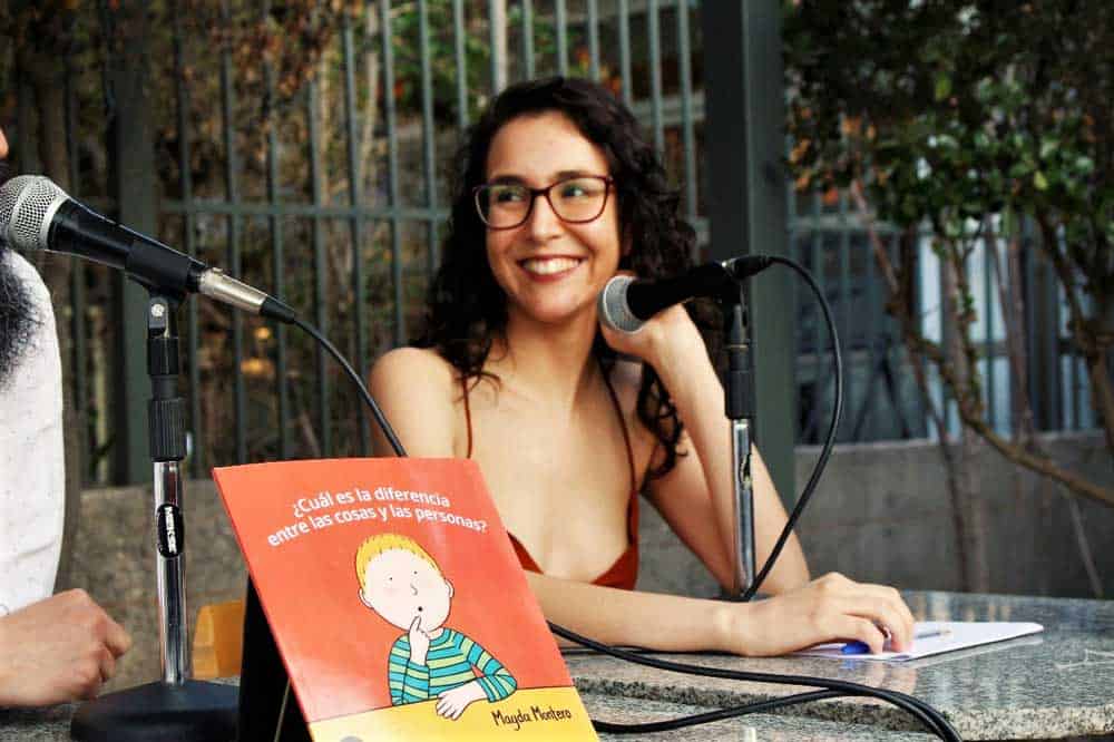 Persona con anteojos y pelo largo sonriendo y un libro delante de ella
