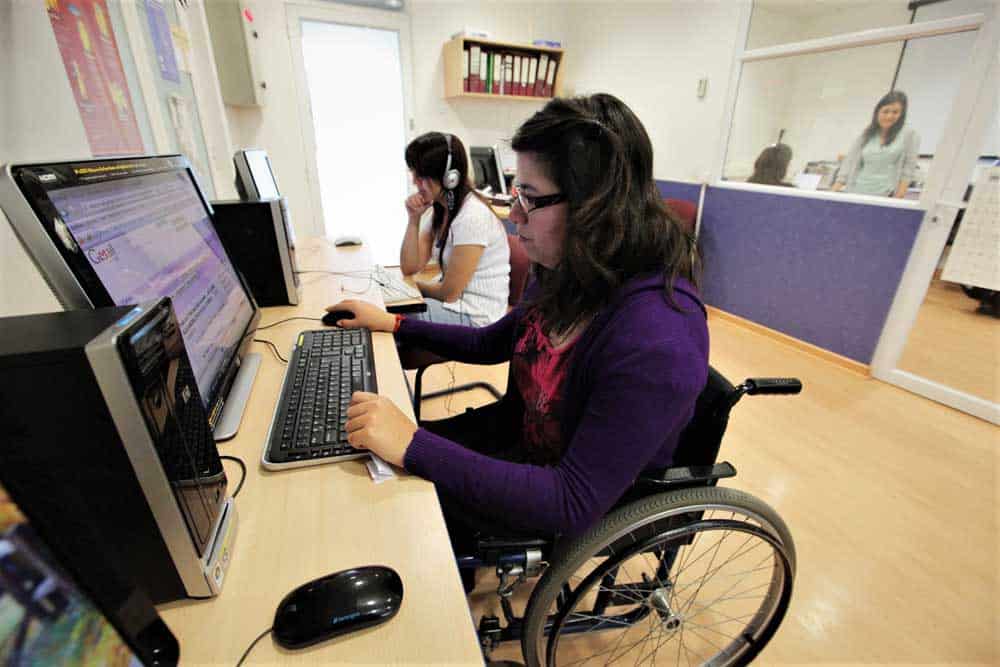 Dos personas frente a computadores, una en silla de ruedas