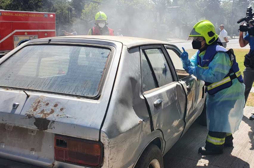 Foto de un simulacro de bomberos donde aparece una bombera comunicandose en señas con una persona dentro de un auto accidentado.
