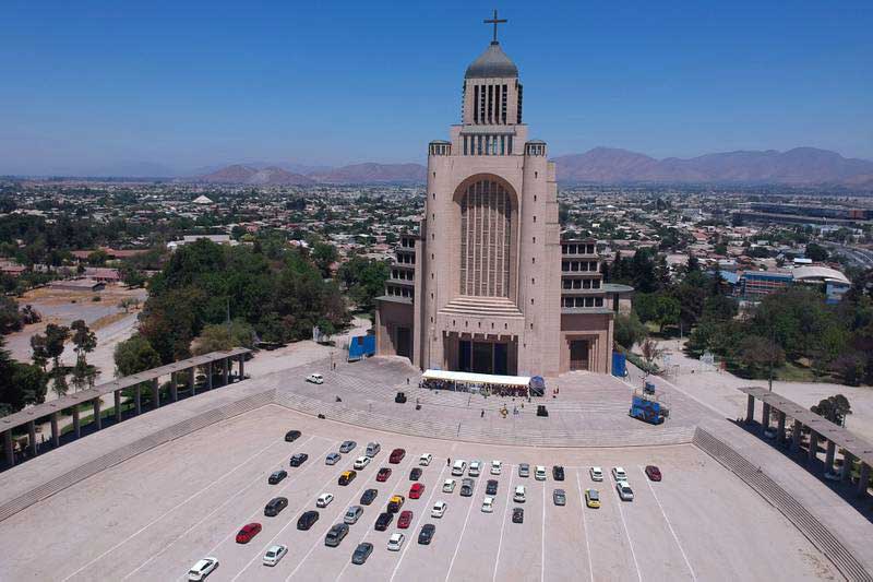 Foto desde el cielo donde aparece el templo votivo de maipú que contiene una gran explanada y al final hay una iglesia muy alta. De fondo se ve la comuna de maipú.