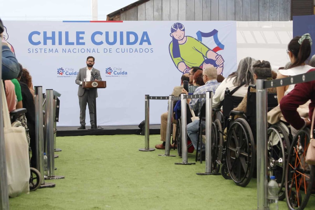 Foto del presidente Boric dando un discurso, y atrás hay un cartel grande que dice: Chile Cuida, Sistema Nacional de Cuidados