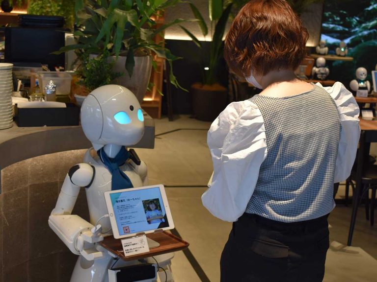 Foto de un robot trabajando como mesero siendo dirigido por una persona con discapacidad desde su hogar.