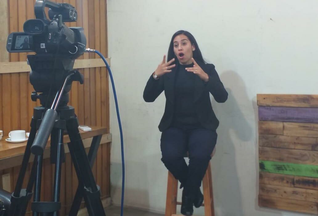 Foto donde aparece una interprete de lengua de señas sentada durante el concejo municipal de castro mientras es grabada con una cámara.