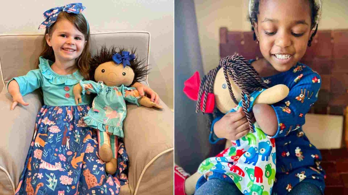 Foto de una niña sin manos sonriendo junto a su muñeca que también tiene solo una mano.