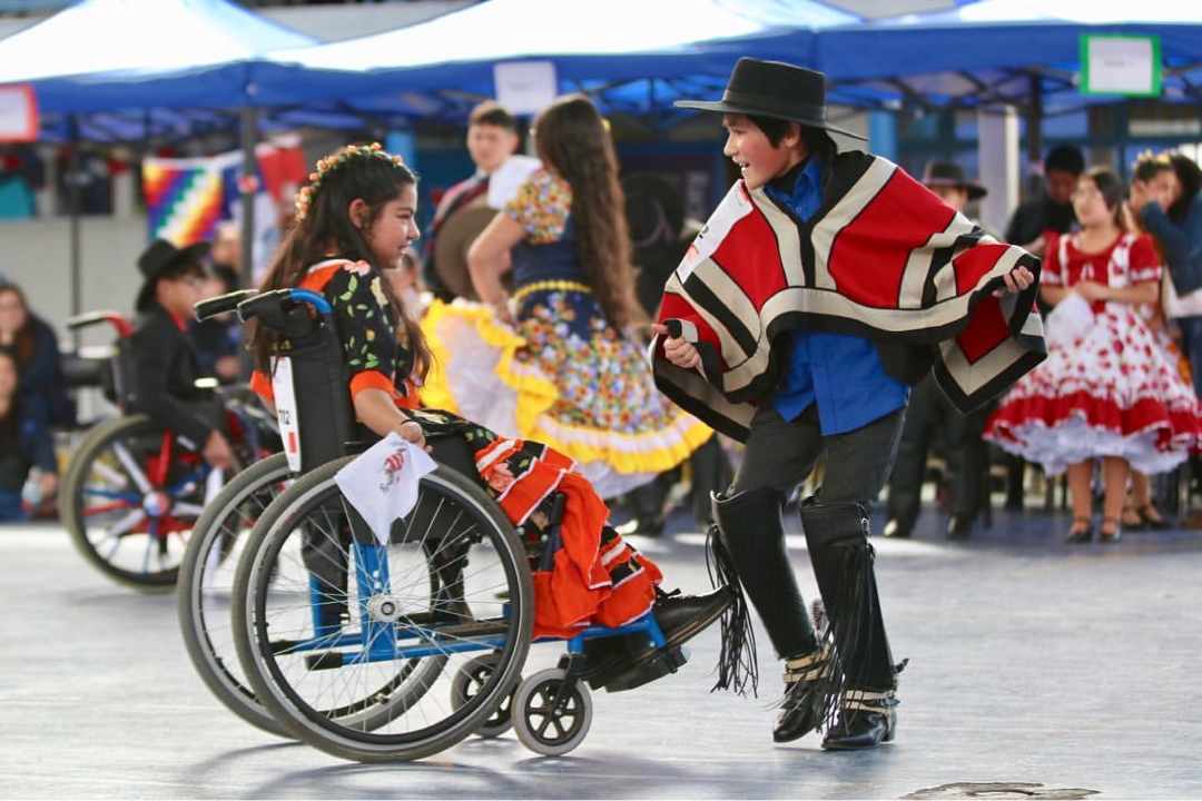 Foto de una niña en silla de ruedas bailando cueca junto a un compañero de baile en su escuela.