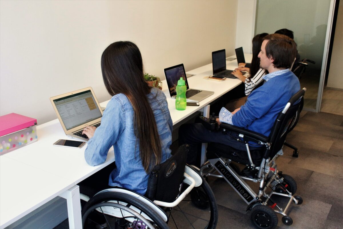 Foto dentro de una oficina donde aparecen algunas personas en silla de ruedas trabajando en sus computadores