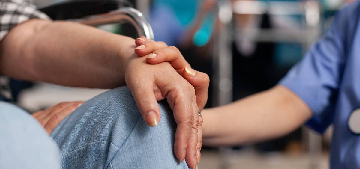 Foto de una persona en silla de rueda recibiendo una mano de otra persona