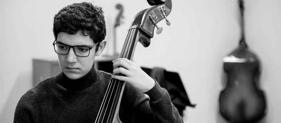 Un joven autista tocando contrabajo y con cara de concentración.