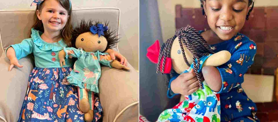 Foto de una niña sin manos sonriendo junto a su muñeca que también tiene solo una mano.