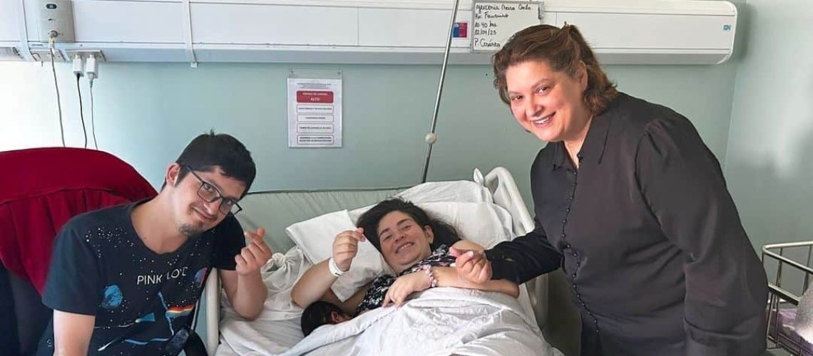 Foto en la pieza de un hospital donde aparece una mujer que acaba de parir acostada en su cama, sonriendo y acompañada de su pareja y al otro lado aparece la intérprete que la acompañó durante el proceso.