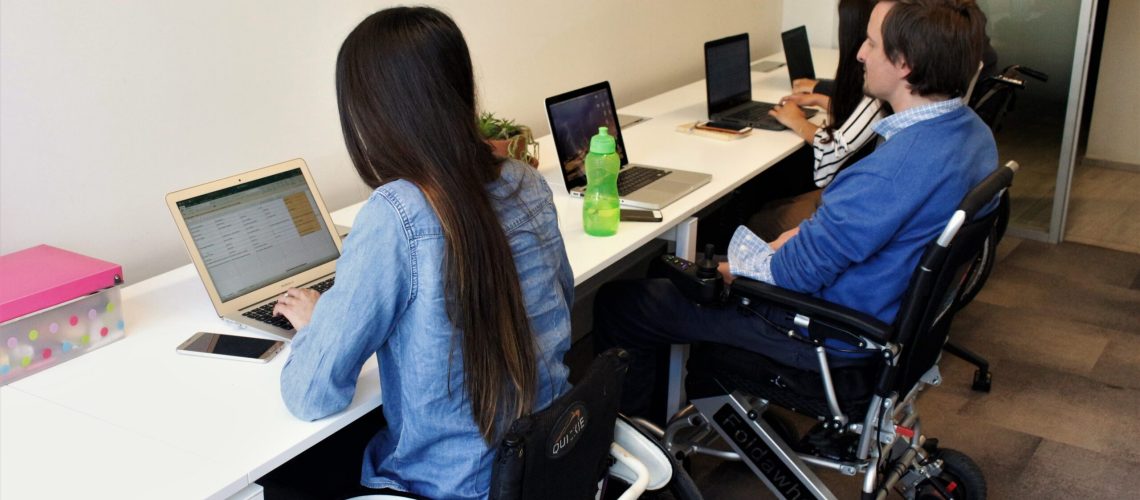 Foto dentro de una oficina donde aparecen algunas personas en silla de ruedas trabajando en sus computadores