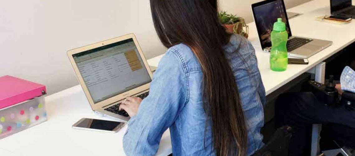 Una mujer en silla de ruedas trabajando en su escritorio con su computador.