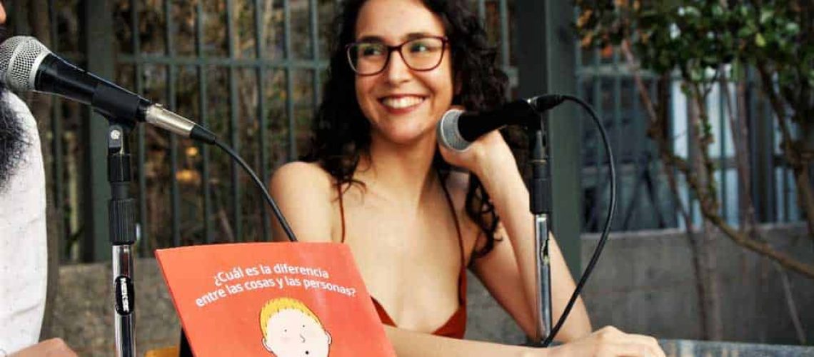 Persona con anteojos y pelo largo sonriendo y un libro delante de ella