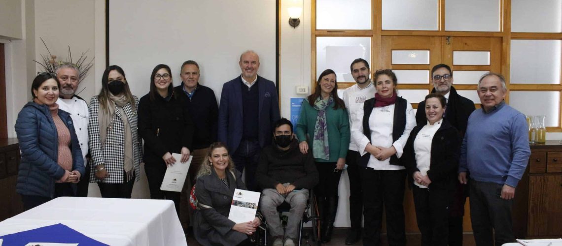 Foto en un salón del colegio achura de las condes donde hay un grupo de 15 personas posando para la foto después de una reunión de trabajo. Una de ellas está en silla de ruedas.
