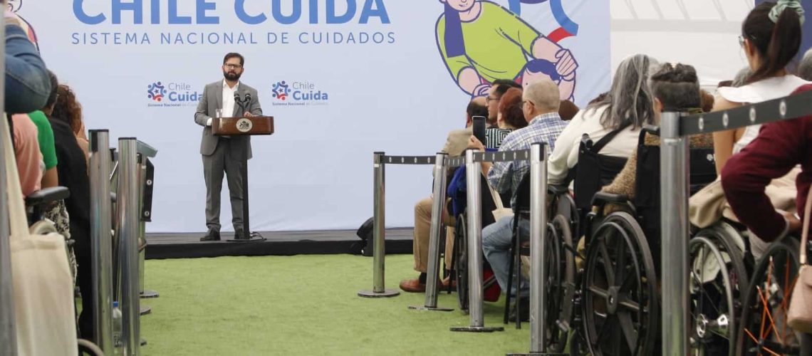 Foto del presidente Boric dando un discurso, y atrás hay un cartel grande que dice: Chile Cuida, Sistema Nacional de Cuidados