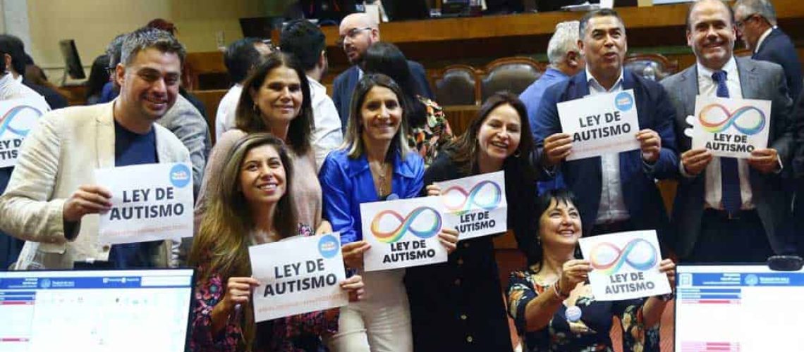 Foto dentro de la cámara de diputados donde aparece un grupo de diputados y diputadas sosteniendo carteles que dicen ley de autismo