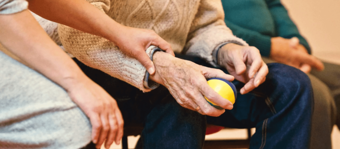 Foto de las manos de una persona con parkinson que está agarrando una pelota de terapia