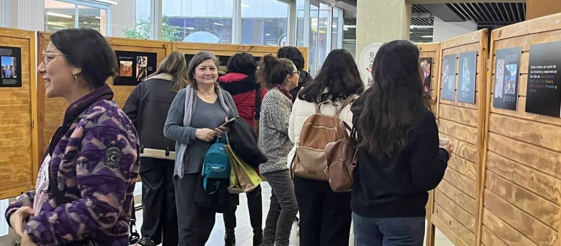 Dentro de un salón, hay un grupo de personas observando detenidamente unas fotos que se exponen en las paredes del lugar.