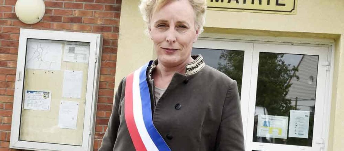 Aparece una mujer trans con una banda presidencial con los colores de Francia. Está afuera de la municipalidad donde trabaja.