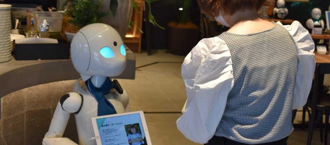 Foto de un robot trabajando como mesero siendo dirigido por una persona con discapacidad desde su hogar.