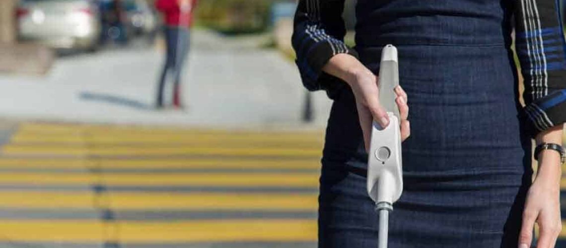Una mujer cruzando un paso peatonal utilizando un bastón que incluye botones con diferentes funciones.