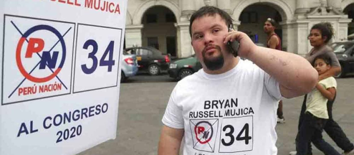 Un joven con Síndrome de Down en una calle en Perú junto a un cartel con su nombre y el número de su candidatura.