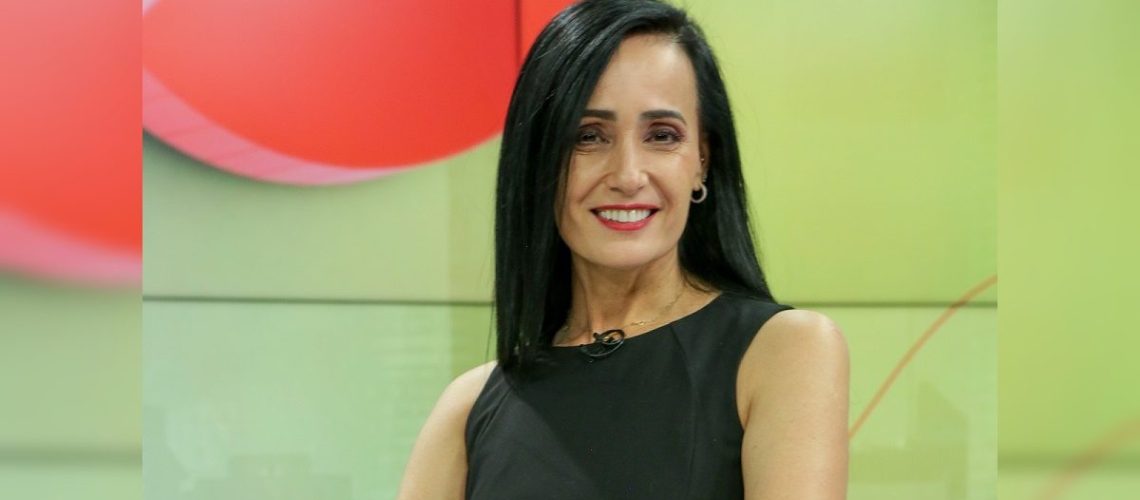 Foto de perfil de la periodista carolina gutierrez quien aparece en un estudio de televisión y sonriendo a la cámara.