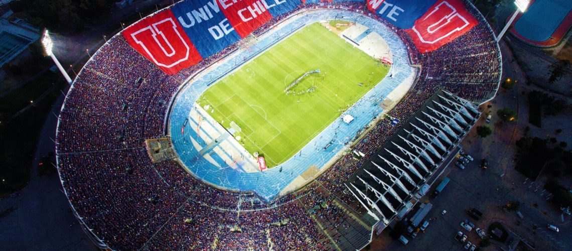 Foto del estadio nacional sacada desde el cielo. Se ve el estadio lleno y la cancha de pasto verde.