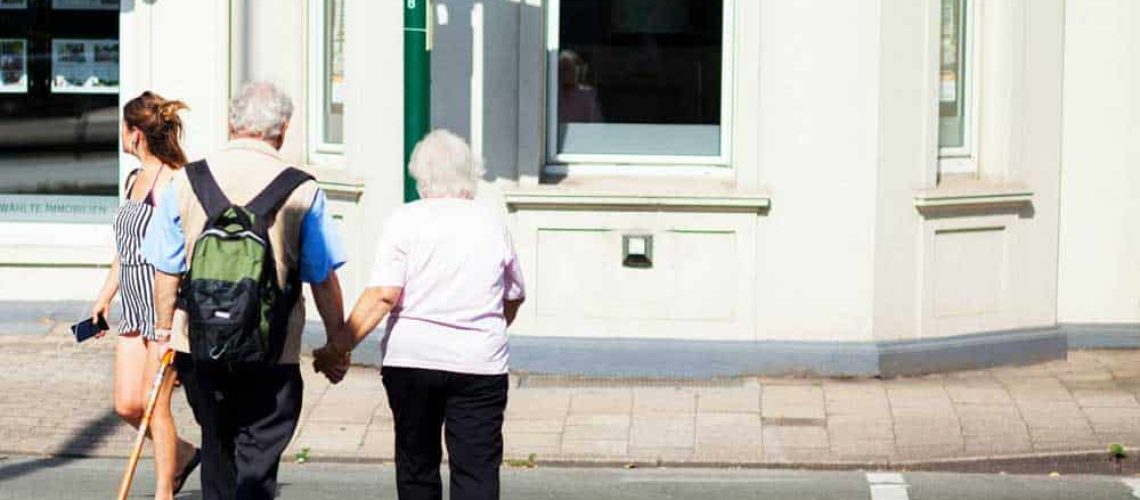 Dos adultos mayores van tomados del brazo mientras cruzan un paso peatonal.