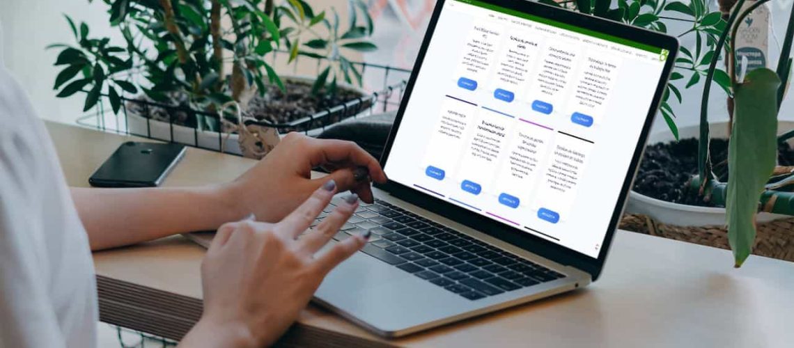 Foto donde aparecen las manos de una persona sentada en un escritorio y con un computador en frente. En el computador está la web de fundacionwazu.cl y sale una lista de diferentes cursos.