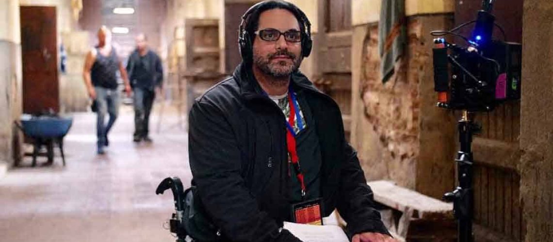 Un hombre en silla de ruedas con audífonos y un guión en la mano durante la grabación de la película "Pacto de Fuga"
