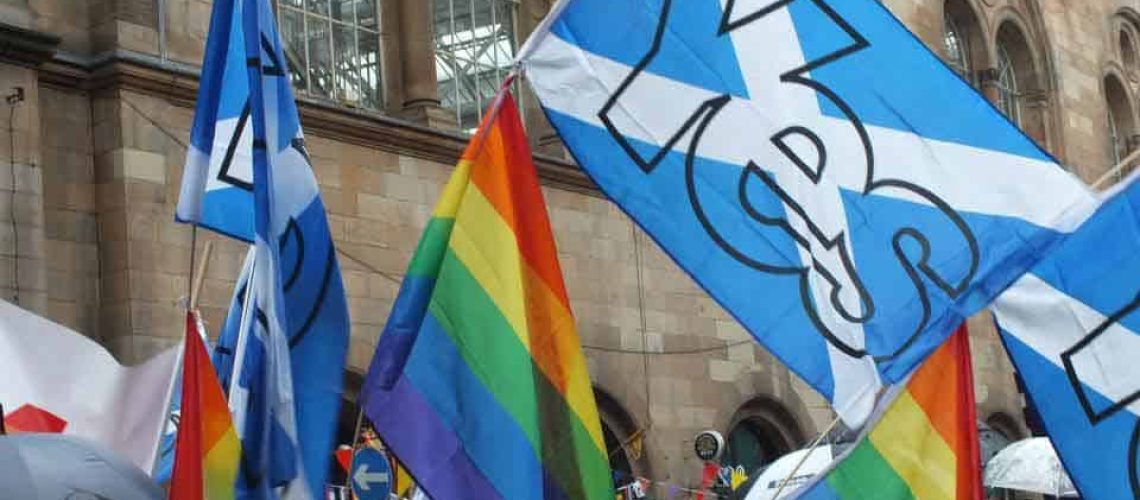 Foto de una manifestación LGBTI en Escocia donde están mezcladas banderas del arcoiris con banderas esocesas.