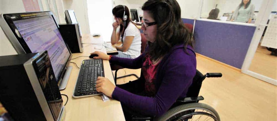 Dos personas frente a computadores, una en silla de ruedas
