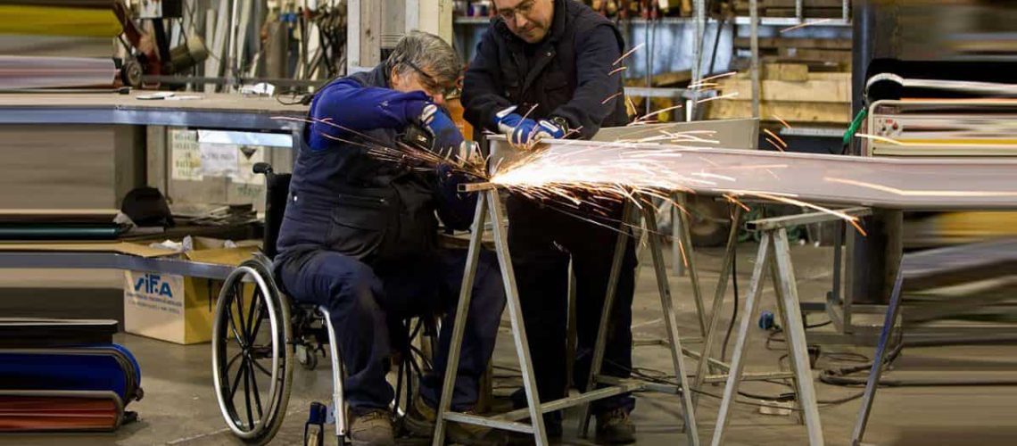 Foto de una persona en silla de ruedas soldando una mesa dentro de un taller.