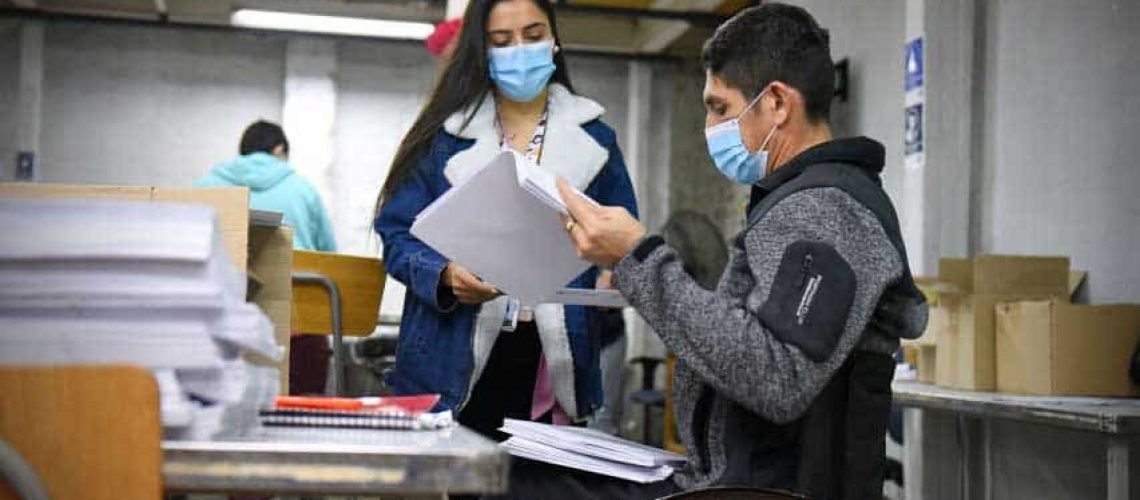 Foto dentro de una oficina donde aparece una persona en silla de ruedas revisando unos documentos y conversando con otra persona.