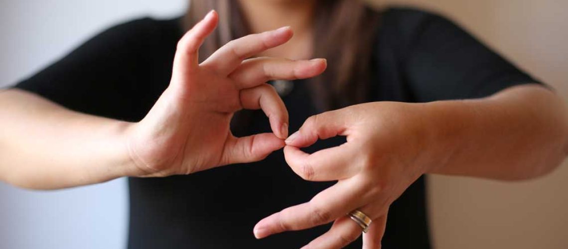 Foto de una intérprete de lengua de señas, y se ve en primer plano sus manos que hacen la seña de interpretación.