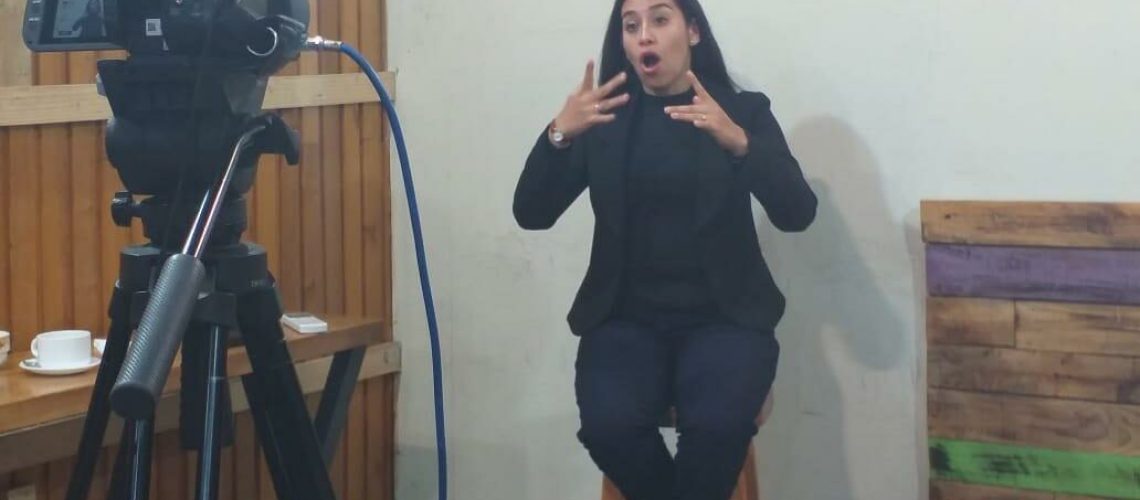 Foto donde aparece una interprete de lengua de señas sentada durante el concejo municipal de castro mientras es grabada con una cámara.