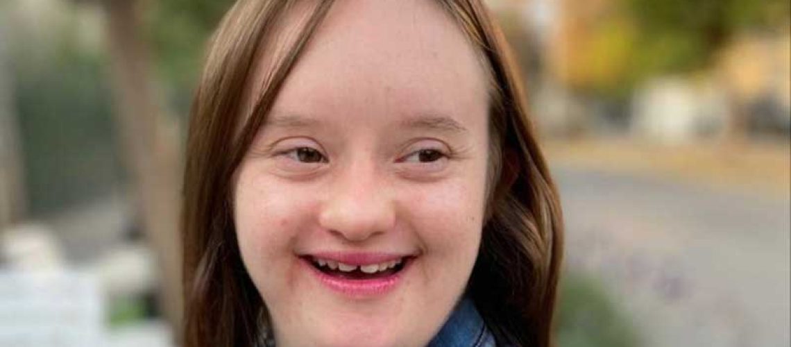 Foto en primer plano de una joven con síndrome de Down sonriendo a la cámara.