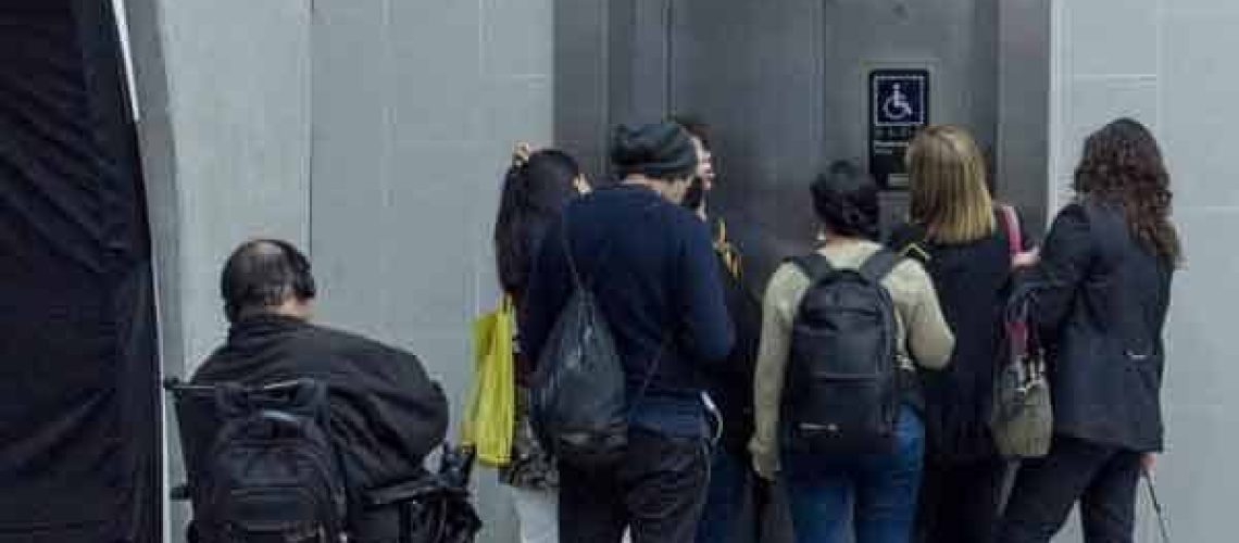 Foto donde aparece una persona en silla de ruedas mirando como otras personas de pie y jóvenes, se suben antes que él.