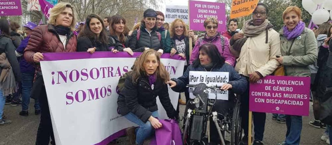 foto de un grupo de mujeres en situación de discapacidad en la calle durante una marcha. La mayoría viste de morado o tiene algún accesorio de ese color. Tienen diferentes carteles y uno de ellos dice "No más violencia de género contra las mujeres con discapacidad".
