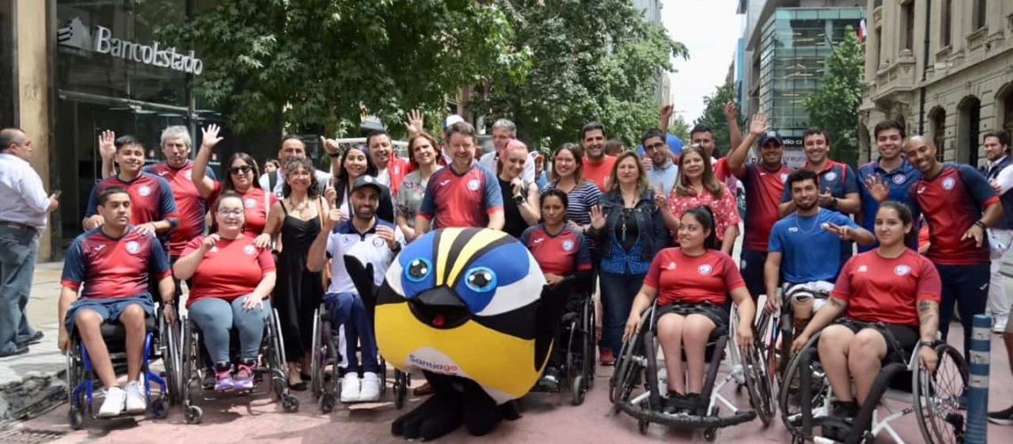 Foto donde aparecec un grupo de deportistas paralímpicos, en su mayoría en silla de ruedas, posando para la foto junto a autoridades y la mascota de los juegos panamericanos.