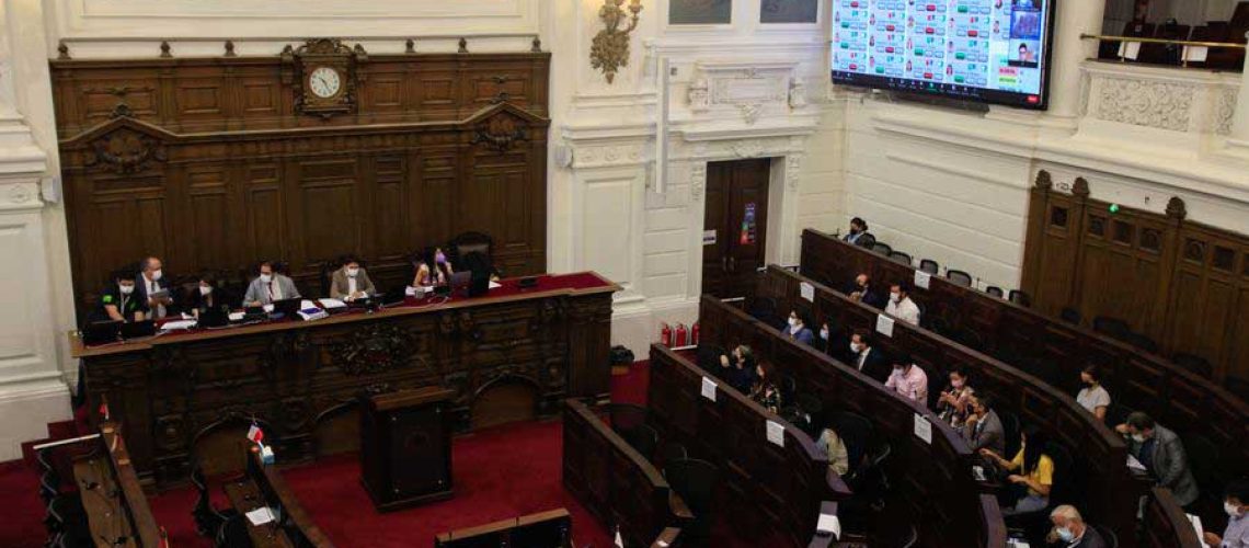 Foto de un salón grande donde se realiza el pleno de la convención constitucional y se ven varios asientos y arriba una pantalla con los resultados de la votación.