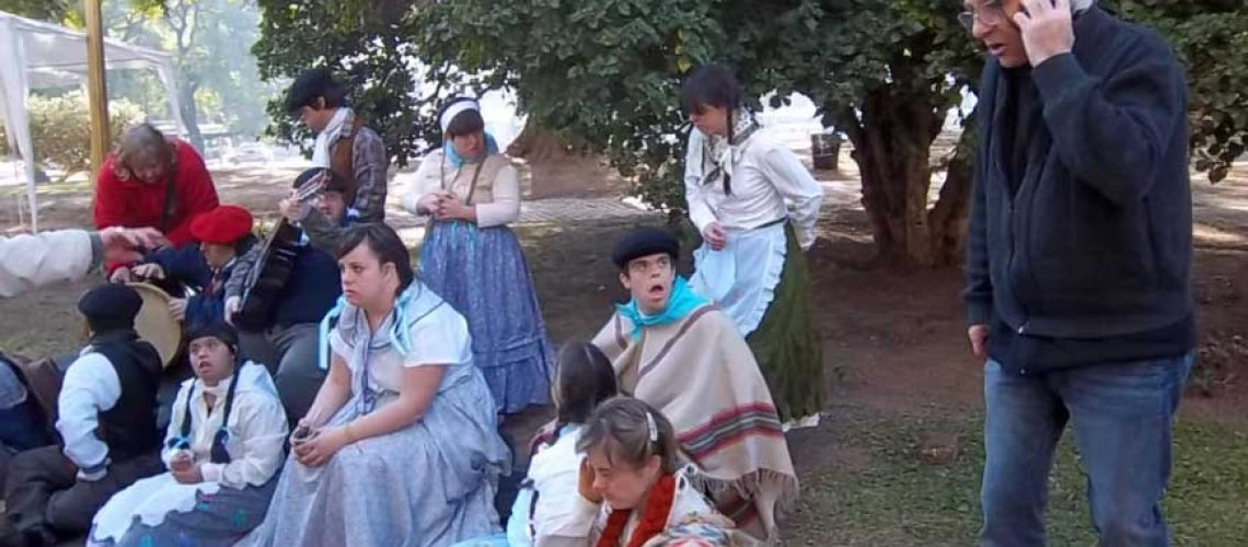 Foto donde aparecen unas 10 personas con algún tipo de discapacidad sentadas en una plaza durante una grabación y con vestimentas antiguas.