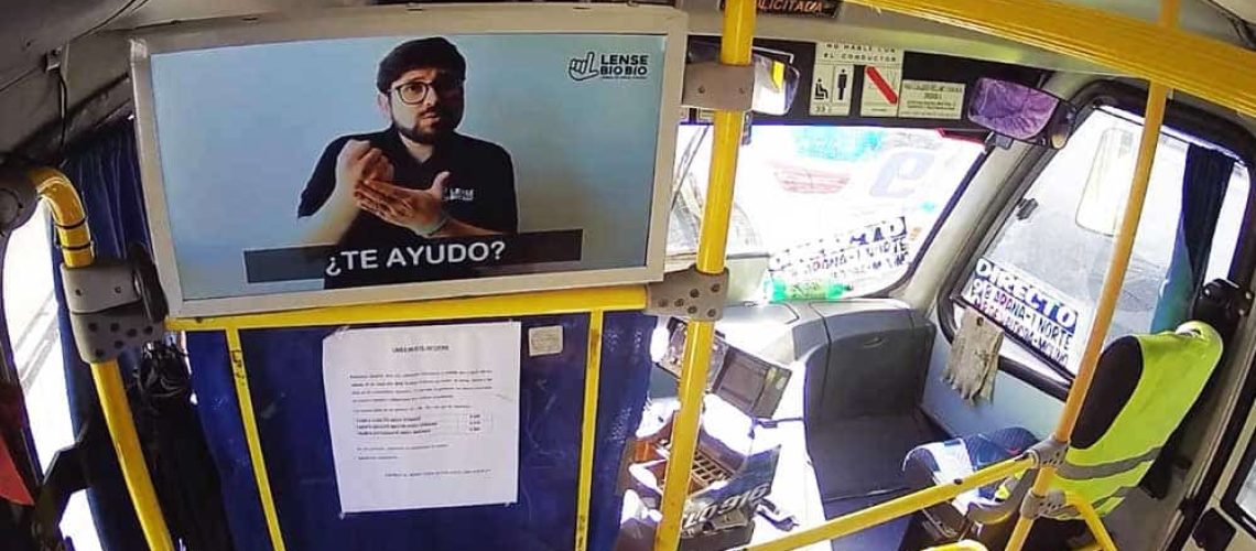 Foto dentro de una micro y en la parte de adelante de la micro hay una pantalla que muestra a una persona enseñando lengua de señas.