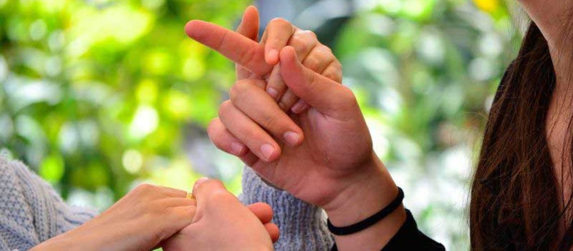 Aparecen las manos de dos personas en contacto directo con la intención de mostrarle una seña a una persona sordociega.