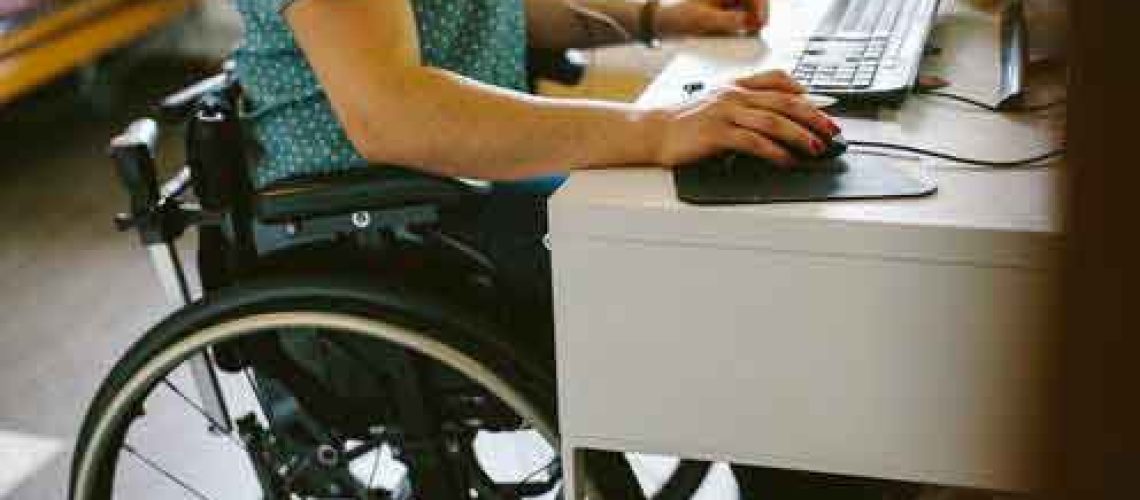 Hay una persona en silla de ruedas trabajando en su computador en su casa.